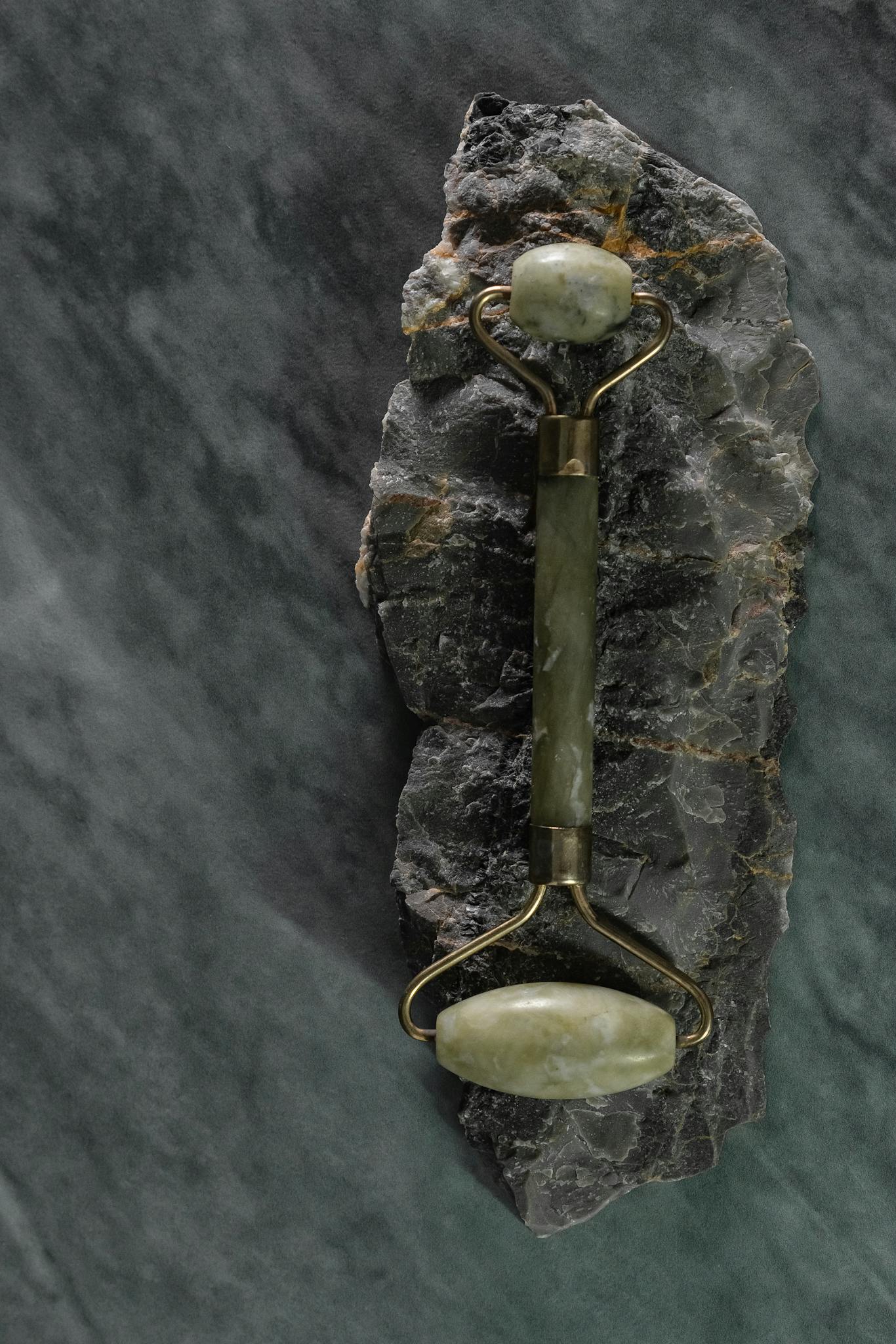 A jade facial roller elegantly placed on a textured marble background for skincare beauty routines.