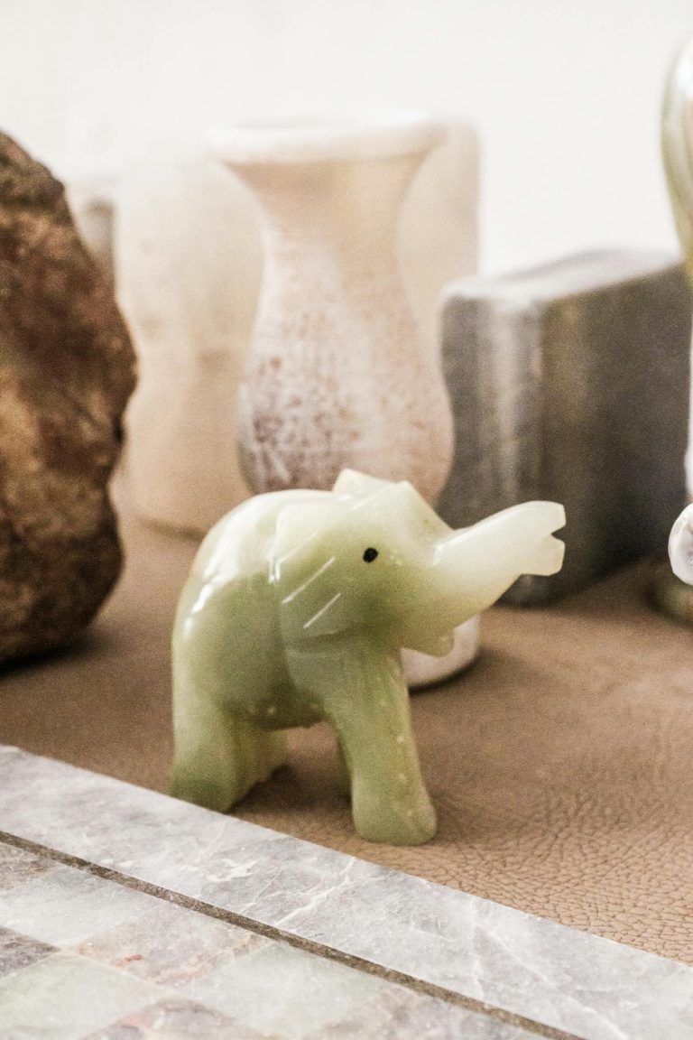 Decorative green jade elephant figurine displayed among ceramic and stone vases indoors.