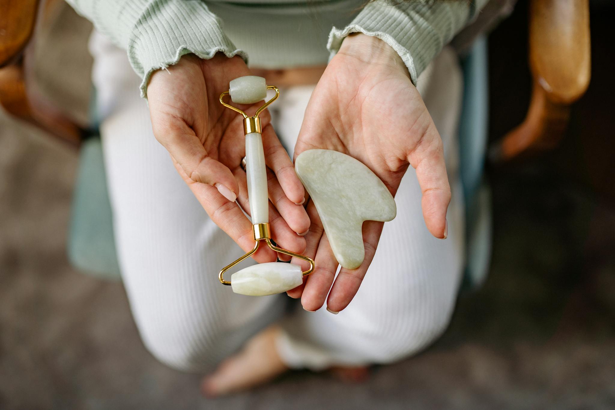 Hands holding jade gua sha and face roller for skin care routines.